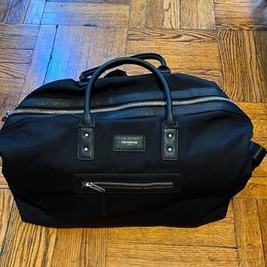 The Kooples black duffel bag with leather handles and chrome zipper.